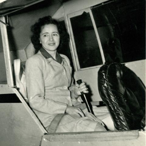 Black-and-white photo of Emma Carter Browning smiling in the cockpit of a small airplane, hand on the control stick.