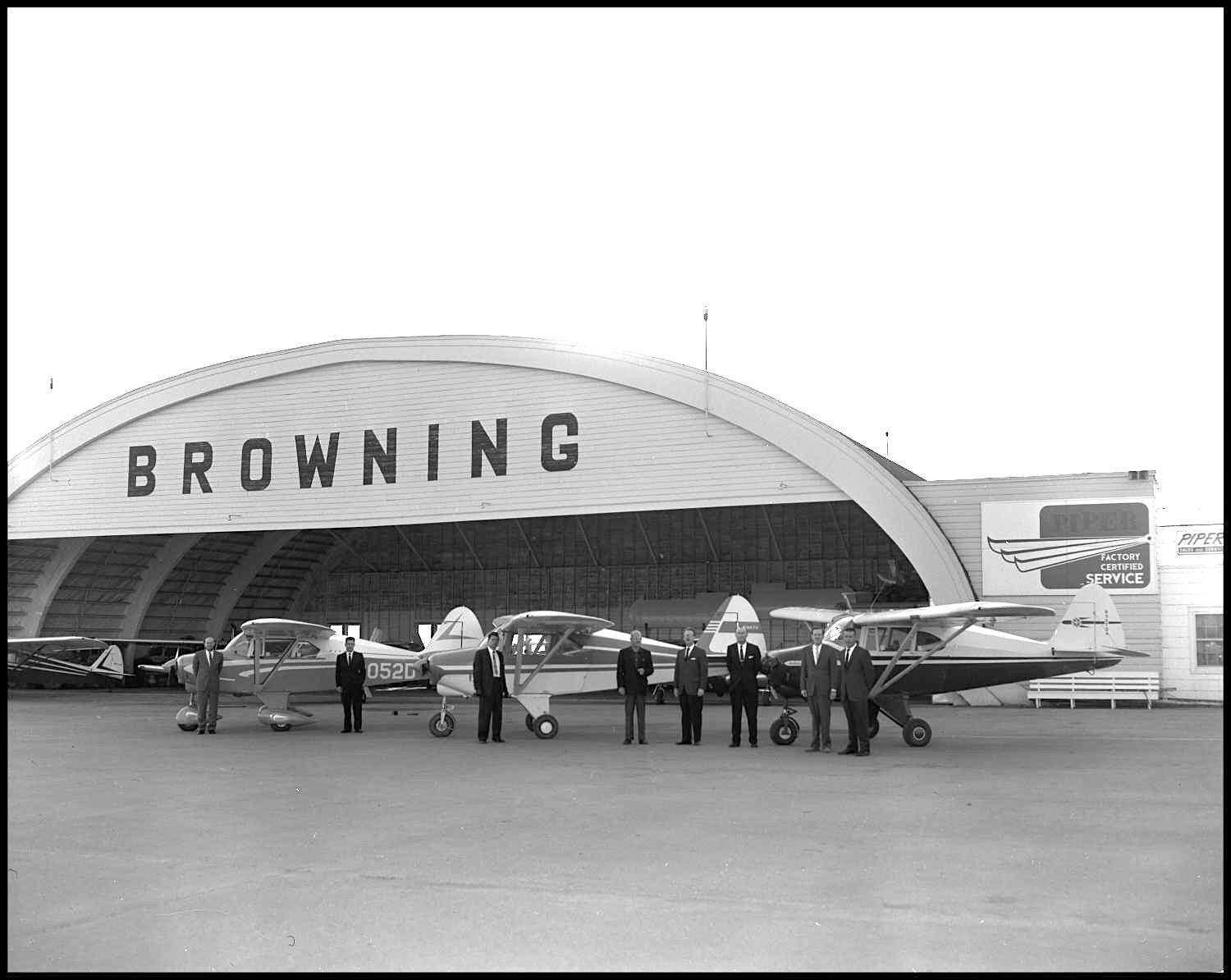 Black-and-white photo of the Browning hangar around 1960, with BROWNING painted on the arch and small airplanes in front.