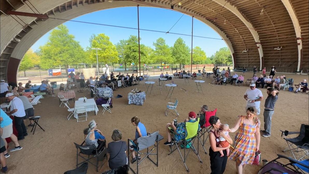 A large crowd seated at tables and chairs under the arches during a community celebration.